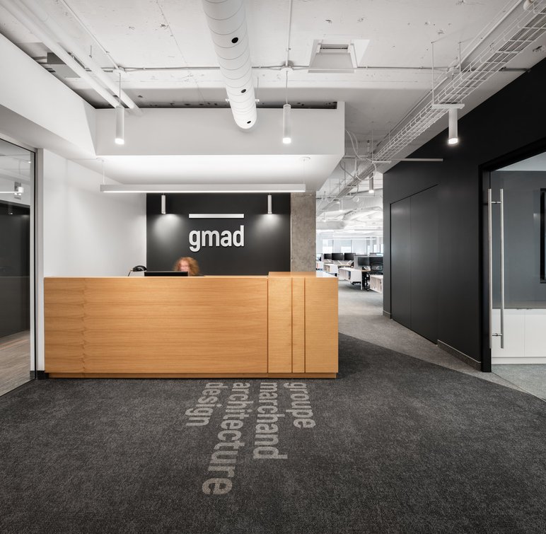 Accueil du bureau de GMAD à Montréal, design intérieur moderne avec réception en bois, mur noir et logo Groupe Marchand Architecture Design