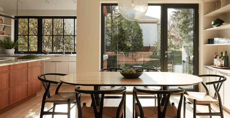 Salle à manger contemporaine de chez Humà Design + Architecture Salle à manger contemporaine avec table en bois clair, chaises noires, cuisine avec armoires en bois et grandes fenêtres donnant sur une cour extérieure de chez Humà Design + Architecture