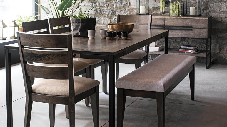 Salle à Manger Rustique et Moderne avec Table en Bois et Métal de chez Ameublement Riquier Salle à manger rustique et moderne avec table en bois et métal, chaises rembourrées et banc assorti, dans un décor en pierre et éclairé par la lumière naturelle de chez Ameublement Riquier.