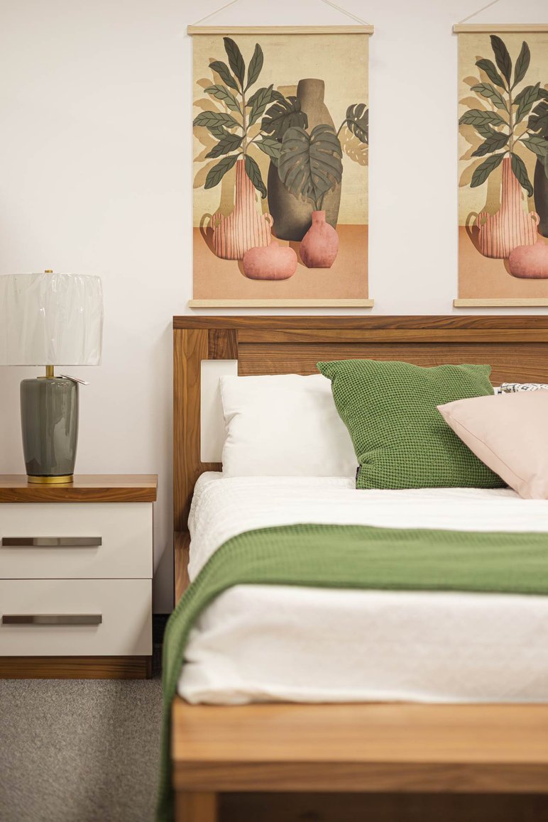 Chambre à coucher moderne avec un lit en bois, des coussins verts et roses de chez magasin Avivia Chambre à coucher moderne avec un lit en bois, des coussins verts et roses, une table de chevet blanche et une lampe élégante, accompagnée de décorations murales artistiques aux tons naturels de chez magasin Avivia.
