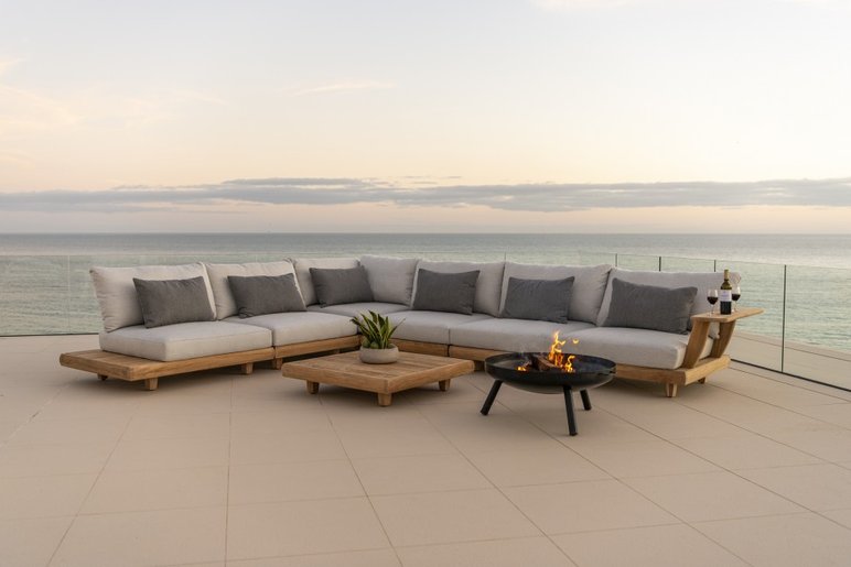 Salon extérieur élégant avec vue sur l’océan de chez JML Inc. Grand canapé d’extérieur en bois avec coussins gris, table basse assortie et foyer au gaz, offrant une ambiance chaleureuse avec une vue imprenable sur l’océan de chez JML Inc.