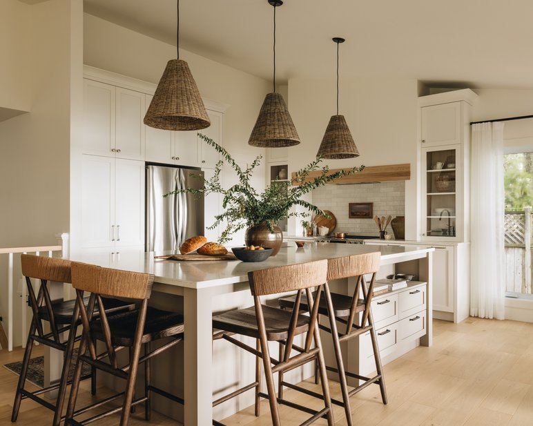 Cuisine lumineuse et chaleureuse avec îlot central en bois clair, chaises en osier, luminaires suspendus en fibres naturelles et décoration végétale, style Maison Olive