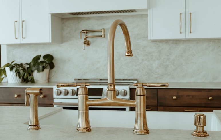 Robinetterie dorée haut de gamme installée dans une cuisine contemporaine avec comptoir pâle et armoires blanches et bois foncé par Plomberie Roy