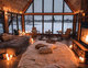 Chambre à coucher grandiose de style chalet avec plafond en bois, grandes fenêtres panoramiques donnant sur un paysage enneigé, éclairage chaleureux et ambiance cocooning par Nikkol sur Pinterest
