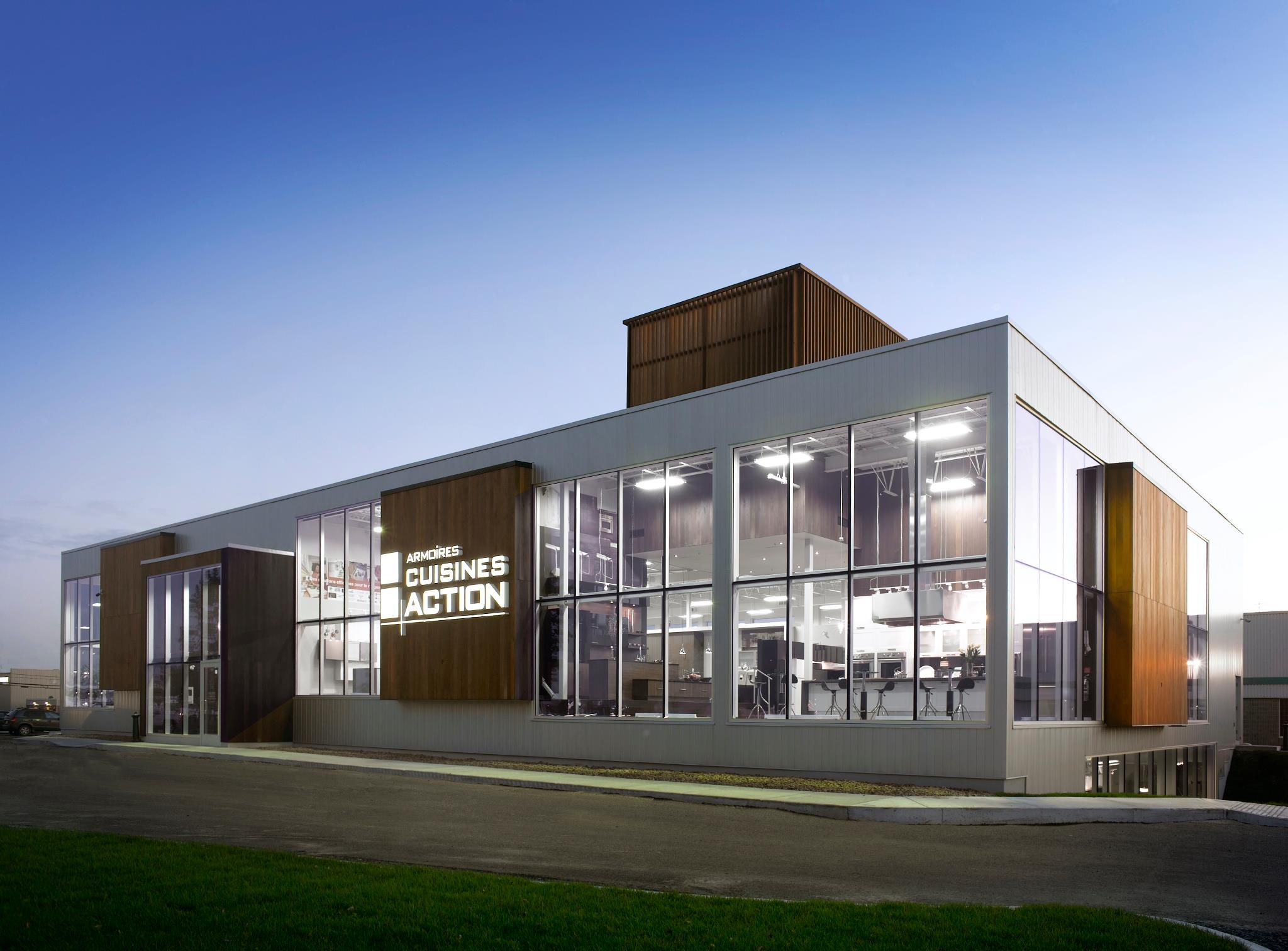 Bâtiment moderne de l’entreprise Armoires Cuisines Action Bâtiment moderne de l’entreprise Armoires Cuisines Action avec façade vitrée illuminée en soirée, spécialisé en armoires et cuisines sur mesure au Québec