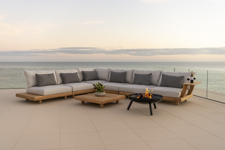 Salon extérieur élégant avec vue sur l’océan de chez JML Inc. Grand canapé d’extérieur en bois avec coussins gris, table basse assortie et foyer au gaz, offrant une ambiance chaleureuse avec une vue imprenable sur l’océan de chez JML Inc.