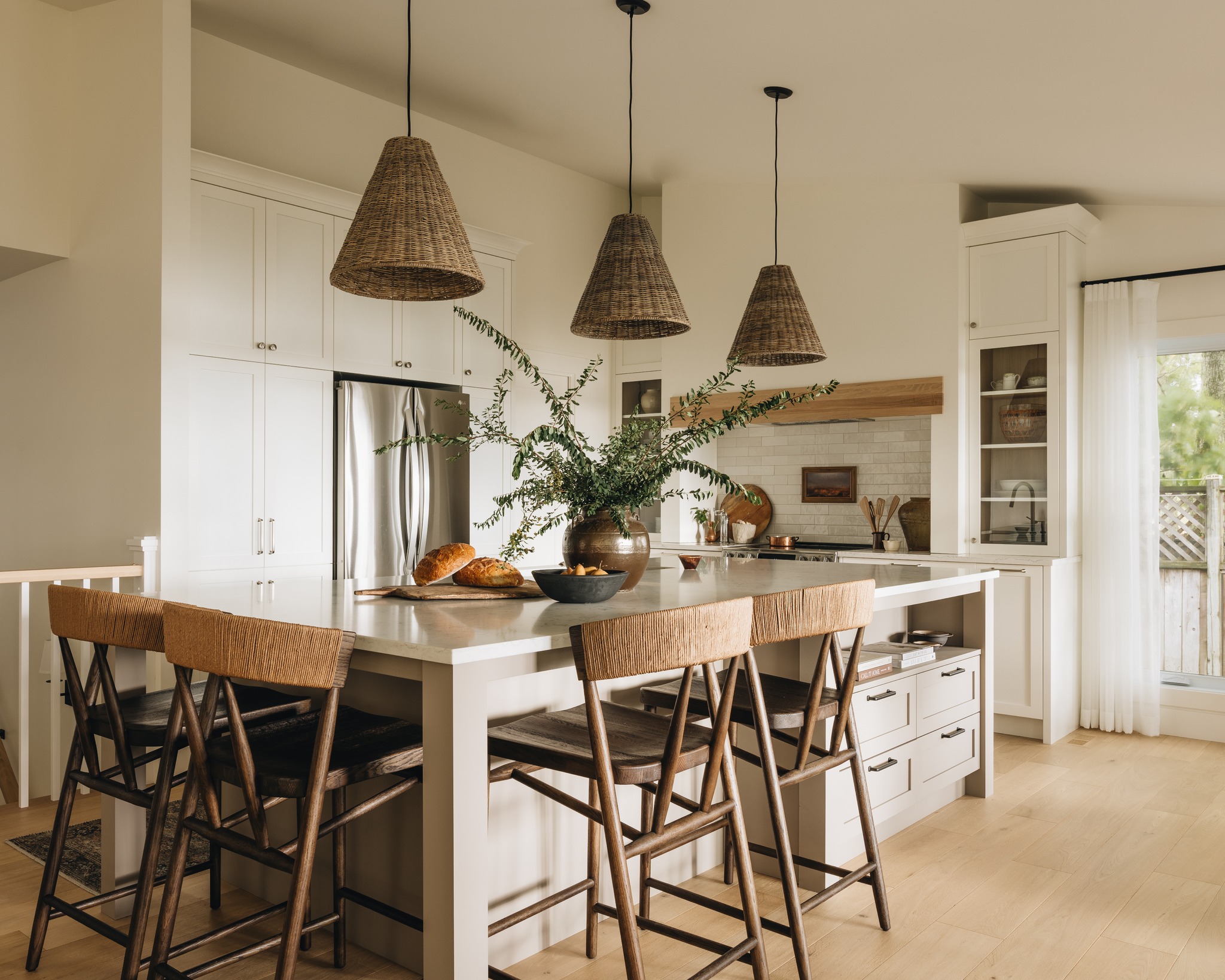 Cuisine lumineuse et chaleureuse avec îlot central en bois clair, style Maison Olive Cuisine lumineuse et chaleureuse avec îlot central en bois clair, chaises en osier, luminaires suspendus en fibres naturelles et décoration végétale, style Maison Olive
